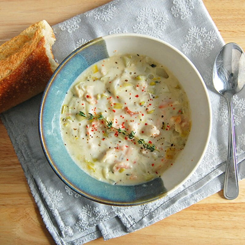 Bol rempli de la chaudrée gourmande du Saint-Laurent garnie avec du thym. Sur une serviette avec une cuillère à soupe et un bout de baguette.