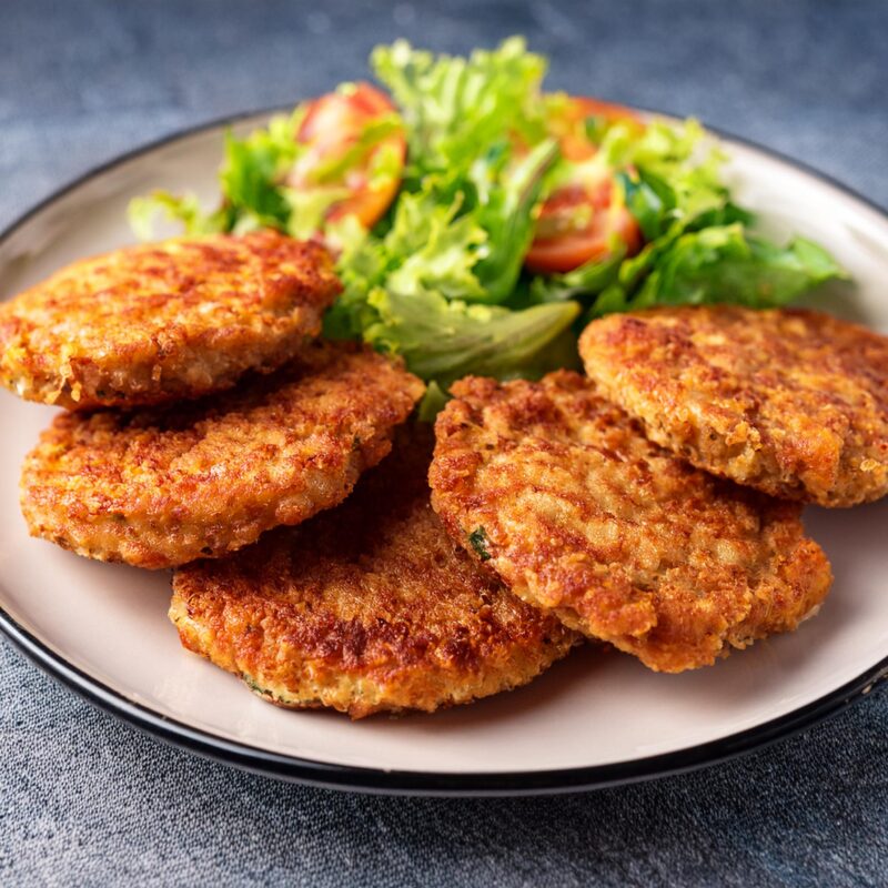Photographie d'une assiette remplie de cinq croquettes plates avec une salade à côté.