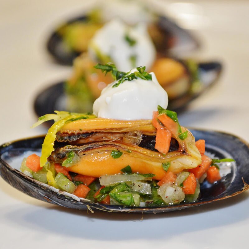 Plan rapproché de la coquille d'une moule qui fait office de bouchée. Moule marnières en coquille avec une crème aux flocons d'algues et des petits légumes.