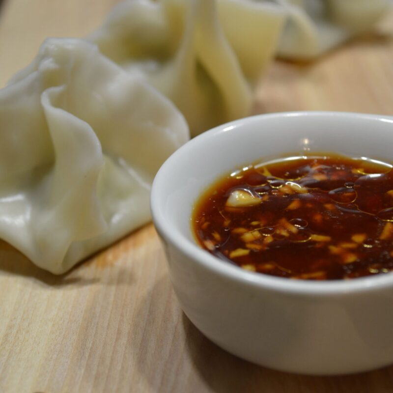 Won tons de flétan avec une sauce épicée au gingembre dans un petit pot sur une planche en bois.