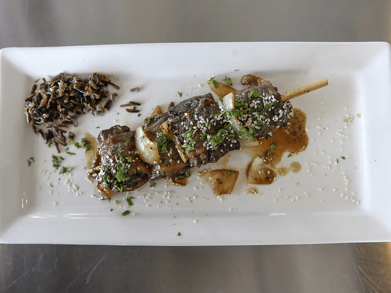 Brochette de loup-marin au sésame avec oignons et herbes aromatique et une sauce brune légère.