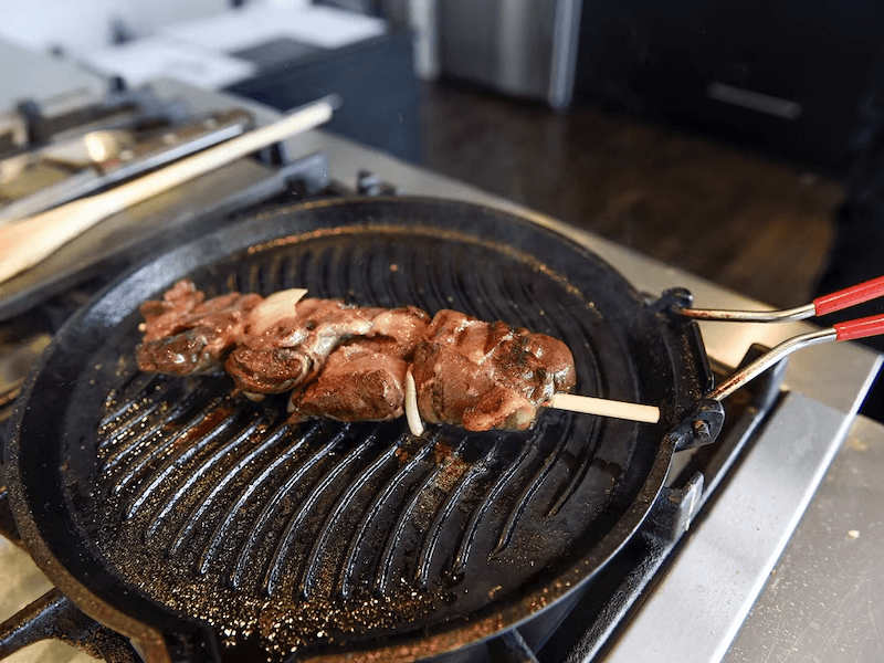 Poêle sur le feu. Avec une brochette de phoque marinée à la sauce Chimichurri en train de griller.