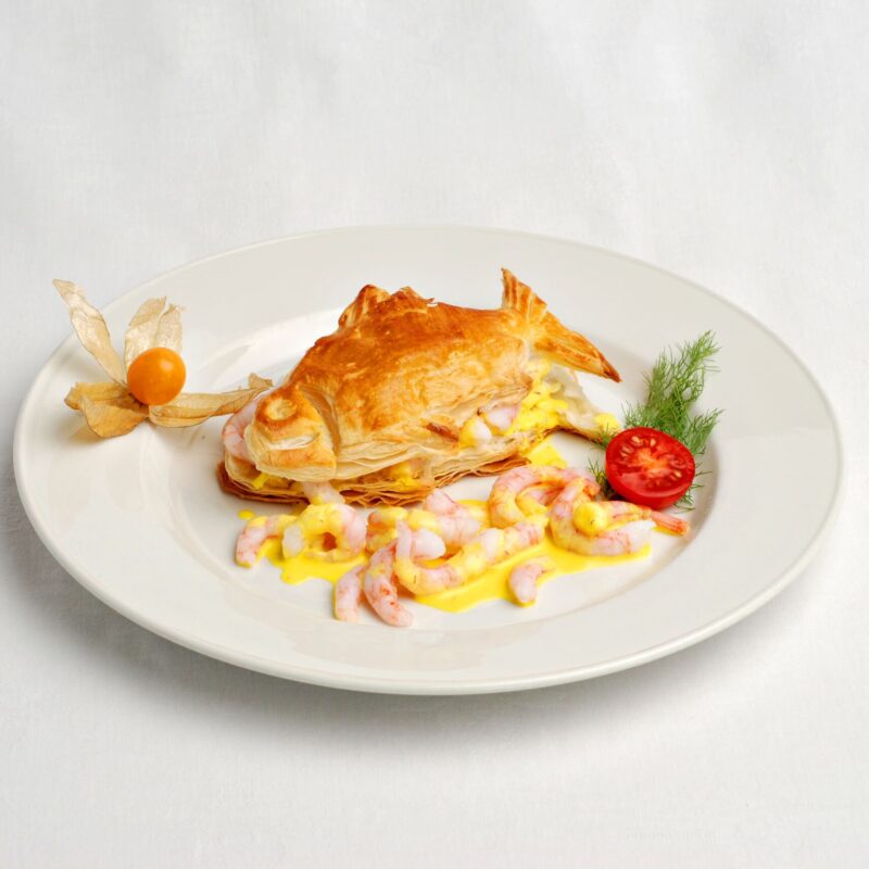 Feuilleté en forme de poisson avec des crevettes nordiques à l'oignon croquant, sauce safran. Accompagné d'un physalis, d'une tomate cerise découpée et de l'annette.