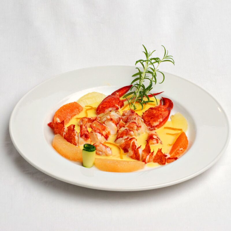 Pinces de homard dans une sauce aux agrumes, avec des agrumes autour et de la courgette en lamelle. Avec du thym.