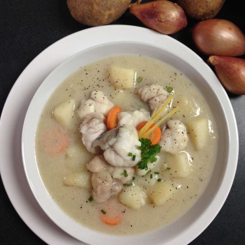 Quiaude gaspésienne dans un bol garni de persil et carottes. En haut à droite de l'échalotte, citron, patates et une feuille de salade.