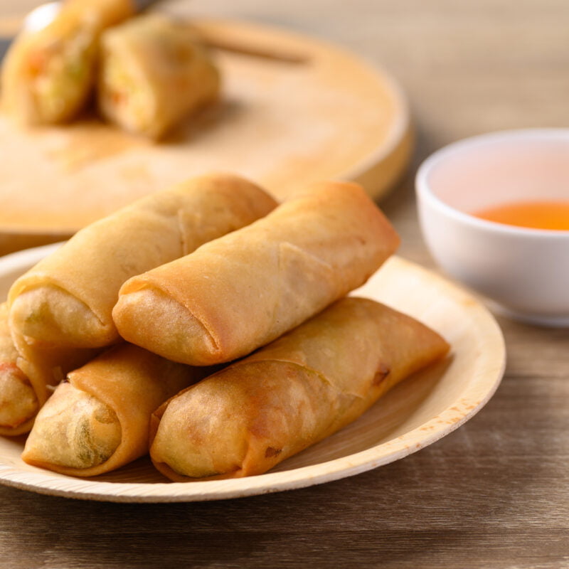 Photographie d'une petite assiette de cinq rouleaux impériaux avec une coupelle de sauce à côté.