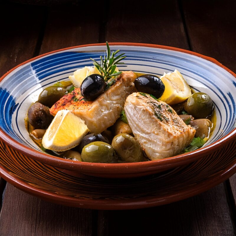 Photographie d'une assiette avec des morceaux de poissons, des olives et du citron.