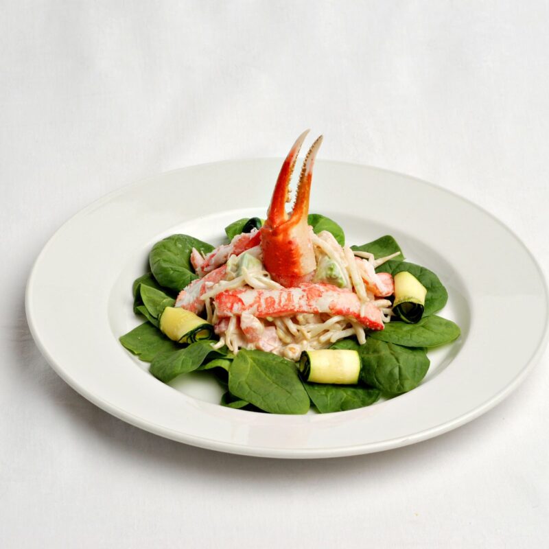 Salade de mâche avec des germes de soya, de la coriandre fraîche et de l'avocat garnie de crabe des neiges avec même la pince sur le dessus de la salade.