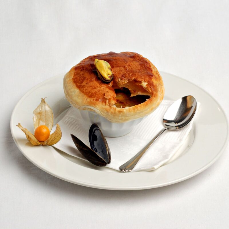 Soupe de moule à la vanille dans un bol avec une croute au dessus et une moule. Accompagné d'un physalis et d'une coquille de moule.