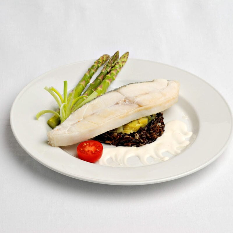 Suprême de Flétan de l'Atlantique au poireau er à l'huile de truffe avec un tomate et des asperges vertes dans une assiette blanche