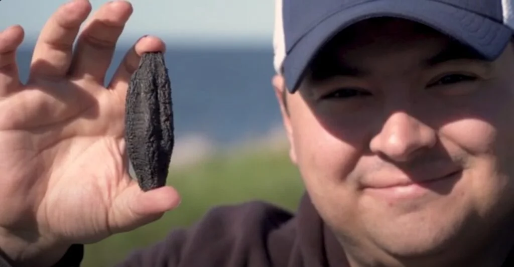 Photo of a man holding a sea cucumber between his fingers, close to his face.
