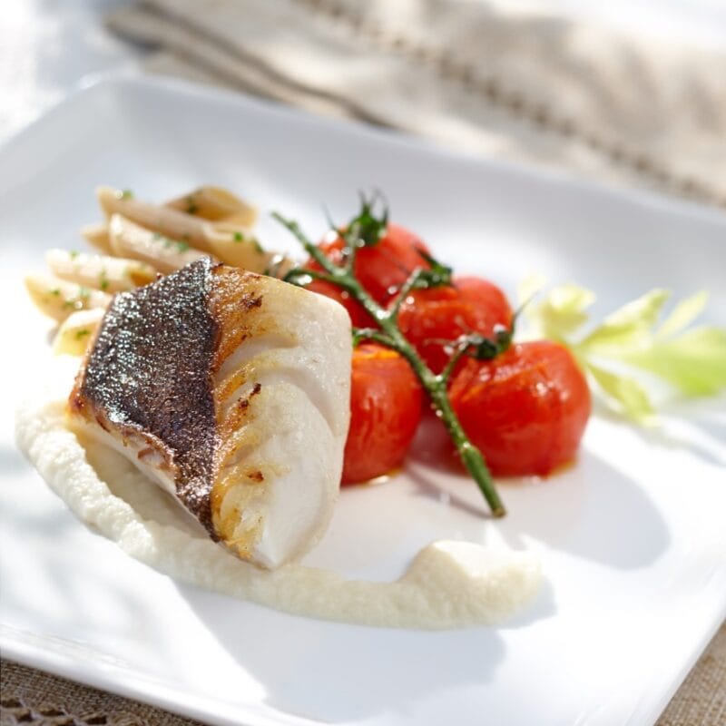 Photographie d'un morceau de poisson blanc posé sur une purée blanche, avec des tomates cerises à côté.