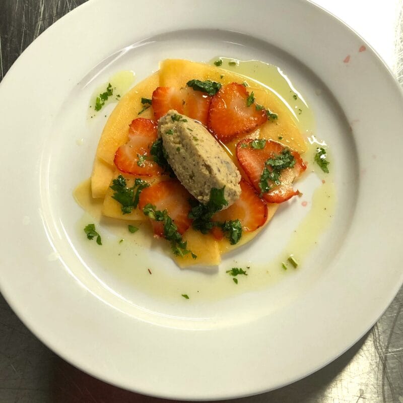 Photographie d'une quenelle de houmous posé sur des fraises tranchées avec de la vinaigrette autour.